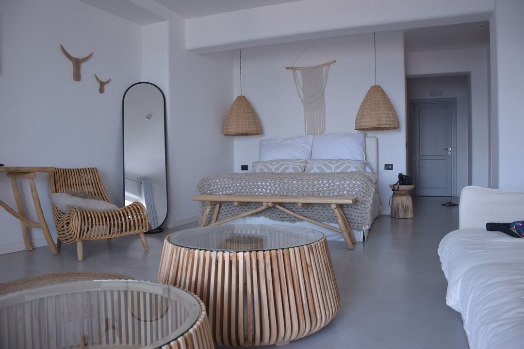 A modern boutique hotel bedroom featuring woven pendant lights, rattan furniture, and neutral tones with natural materials.